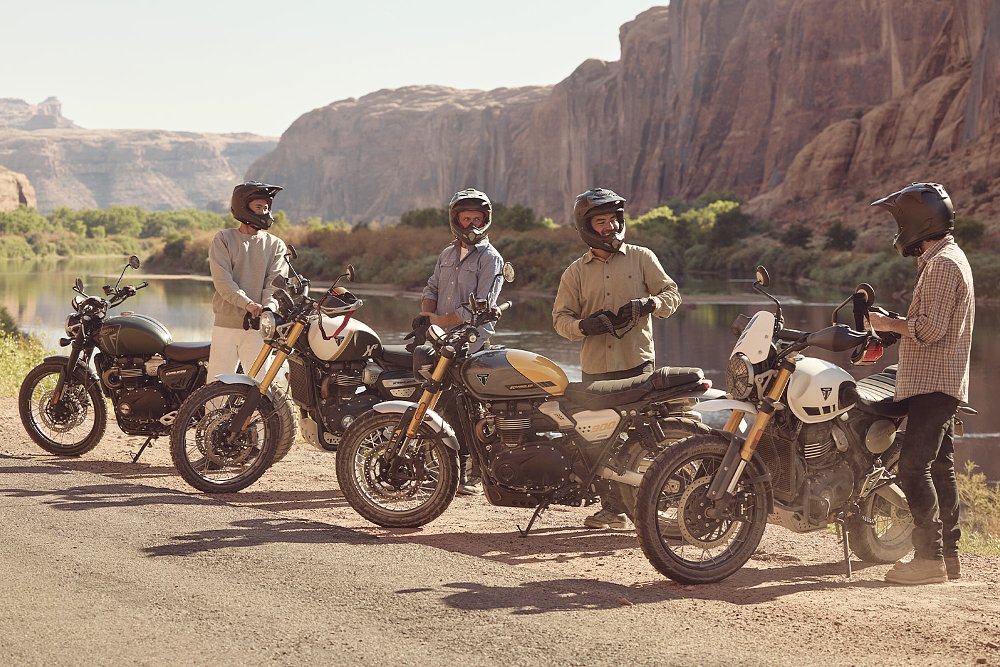 A collection of Triumph Scrambler 900 and Scrambler 1200 XE riders standing roadside.